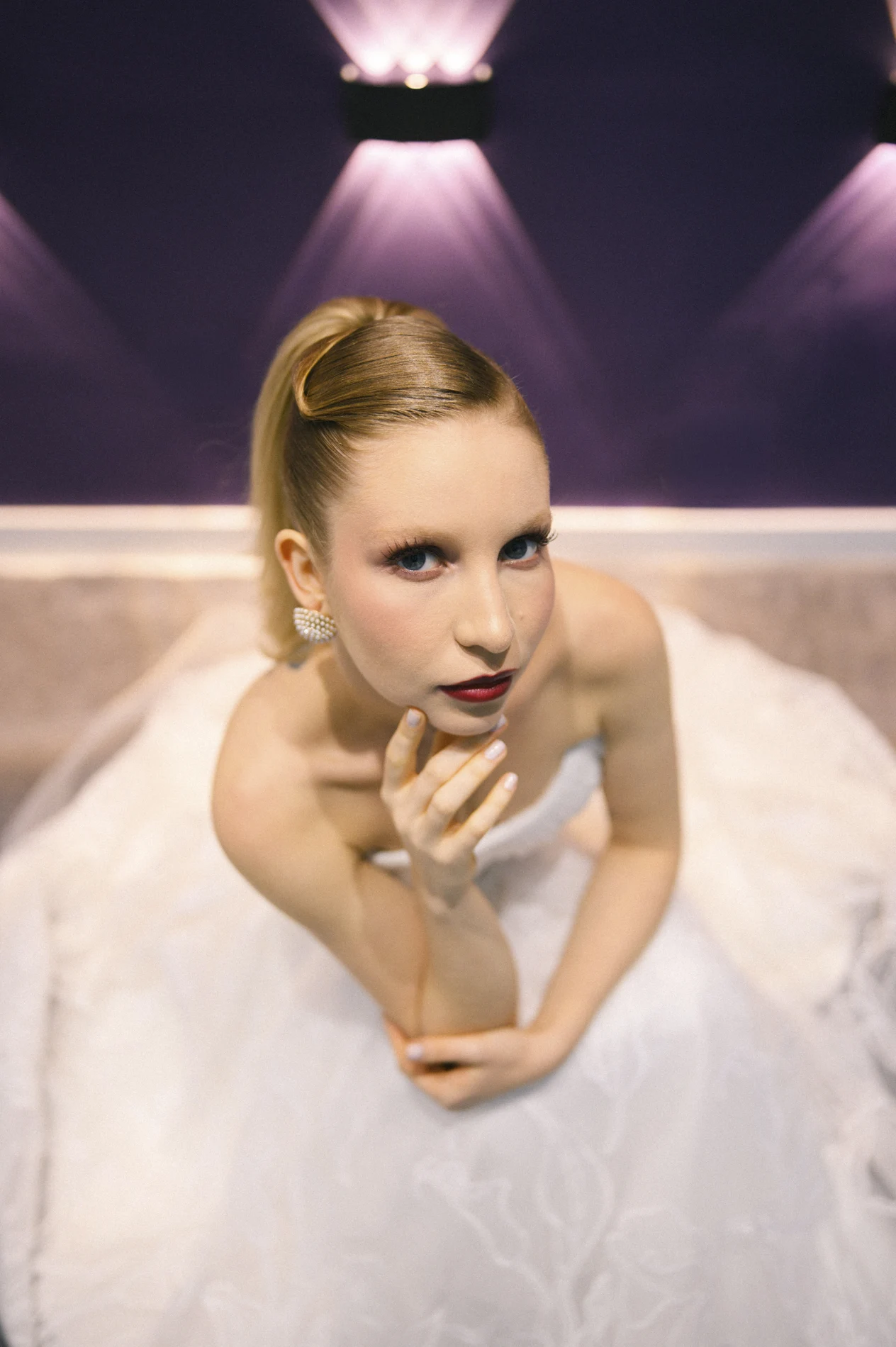 Beauty portrait with a blonde high updo under purple lighting.
