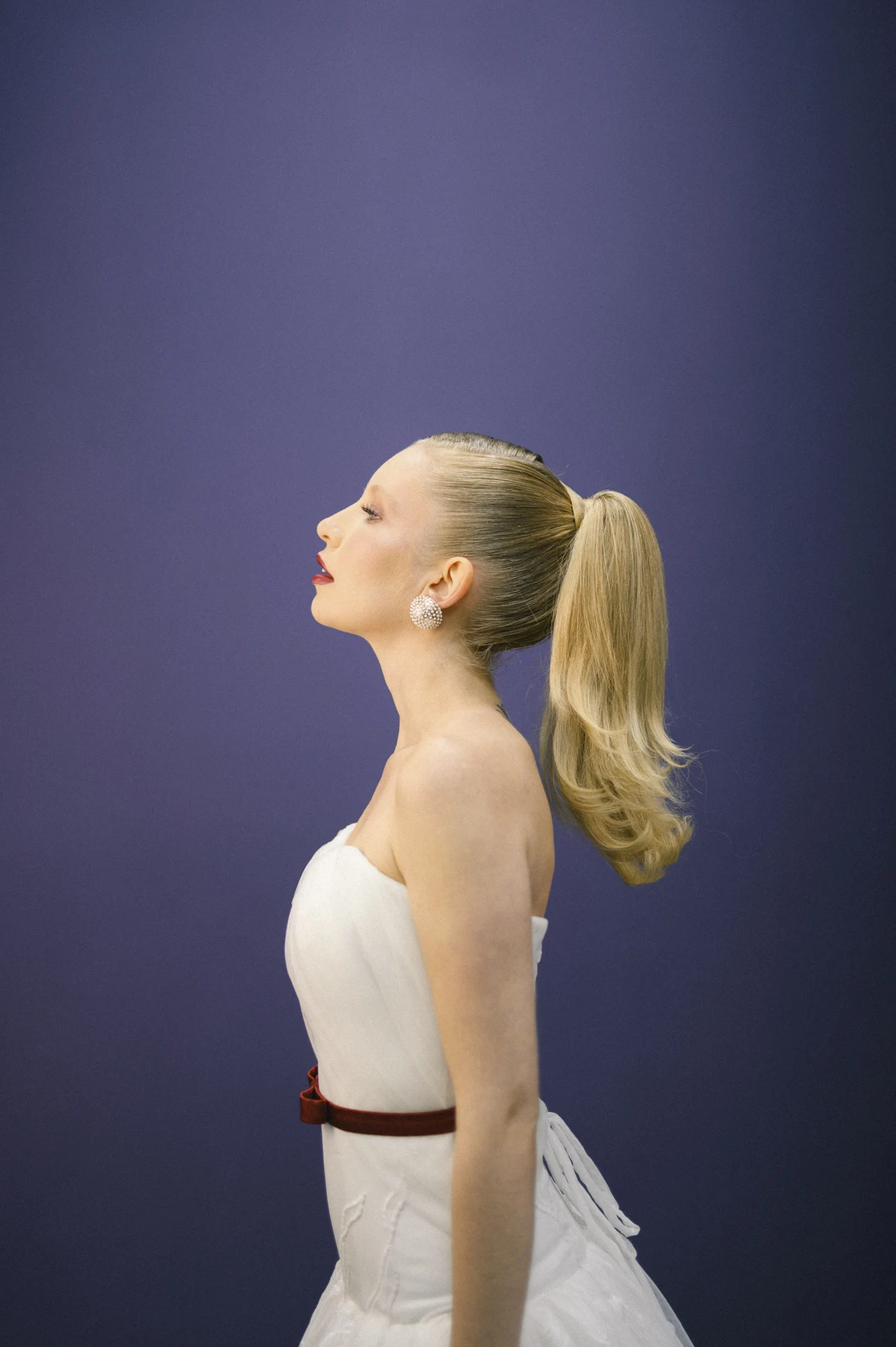 Blonde high ponytail in profile against a purple background.