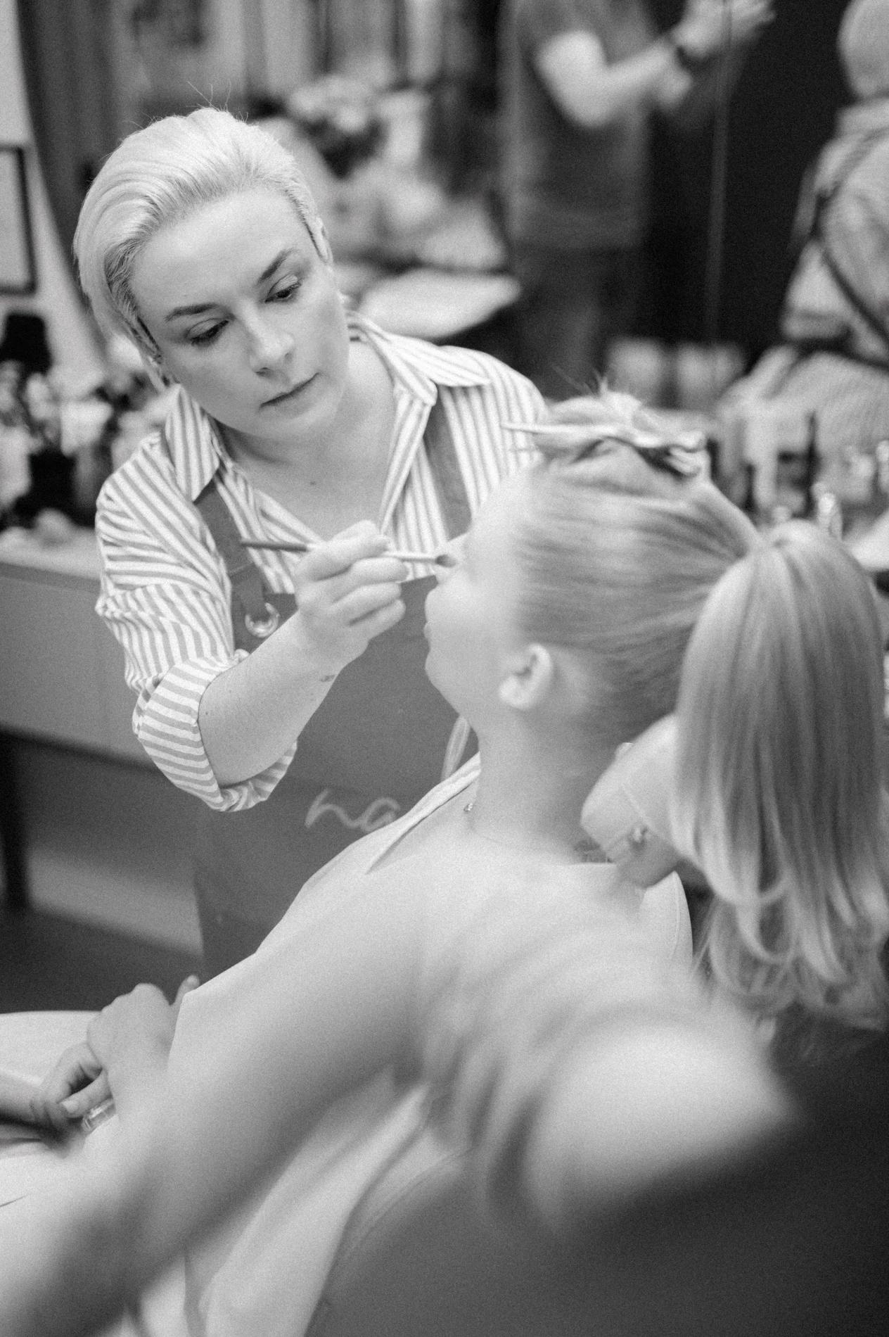Nadia Alves applying makeup to a model, photographed in black and white.