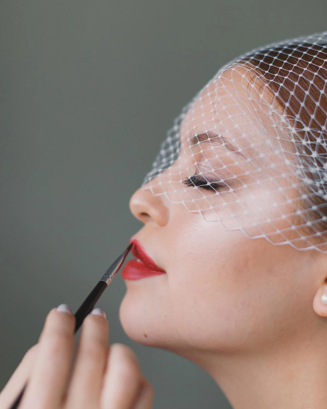Close profile with a birdcage veil and red lipstick being applied.