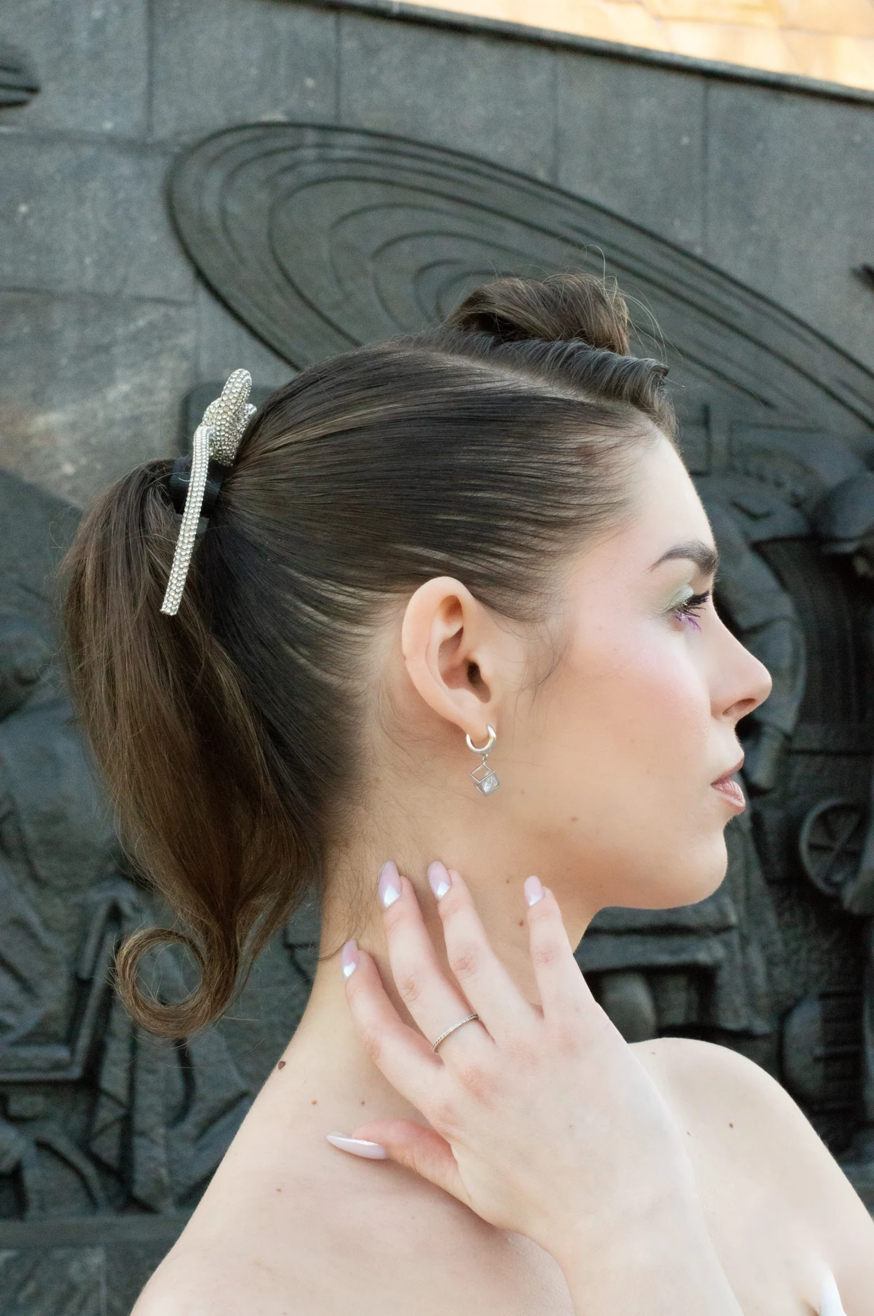 Profile portrait with swept-back hair, a pale ribbon, and soft makeup.