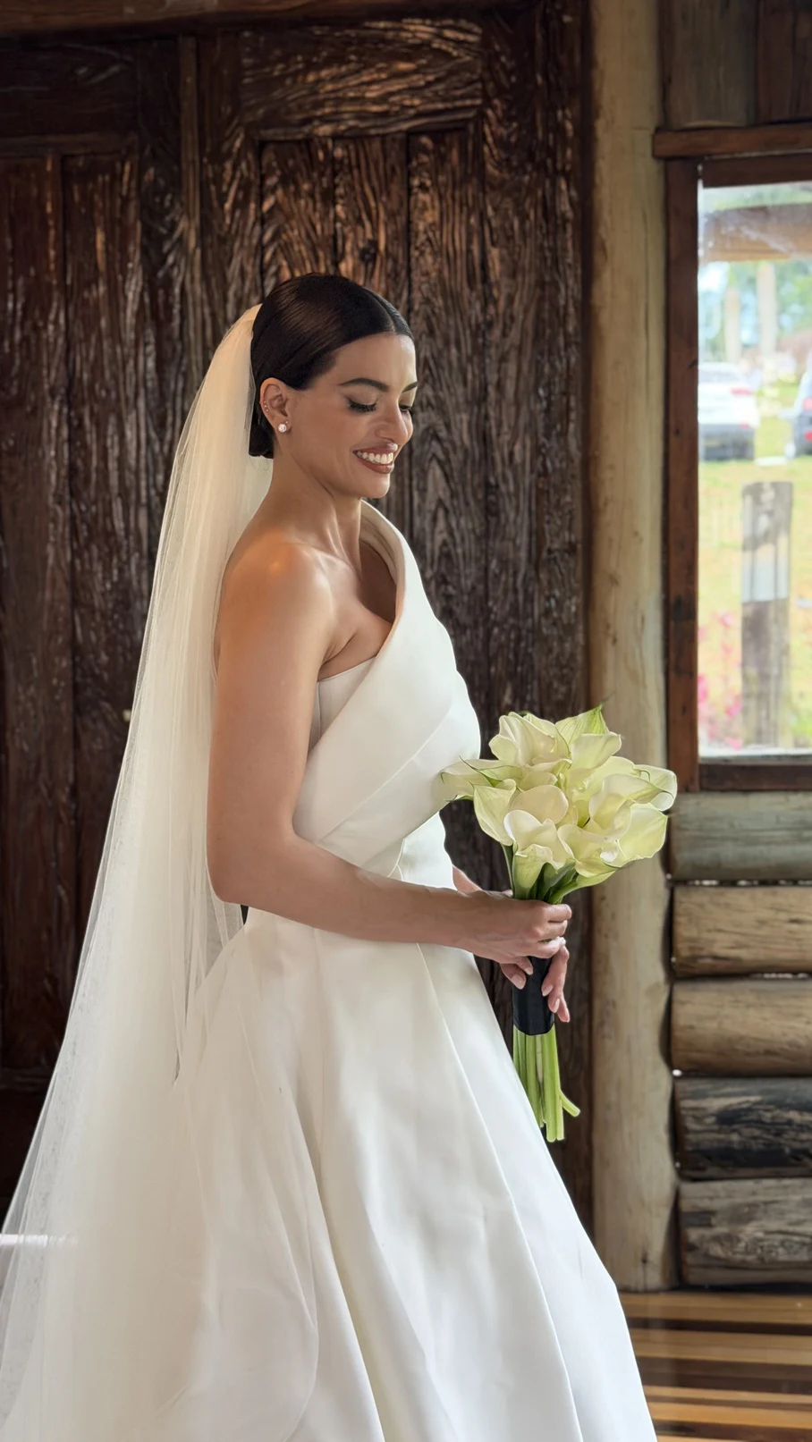 Bride with a white dress and bouquet in front of a wooden door.