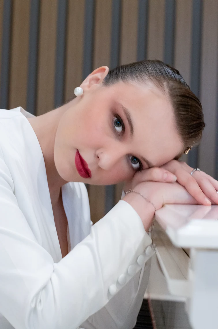 Portrait with swept-back hair and hands resting beneath the face.