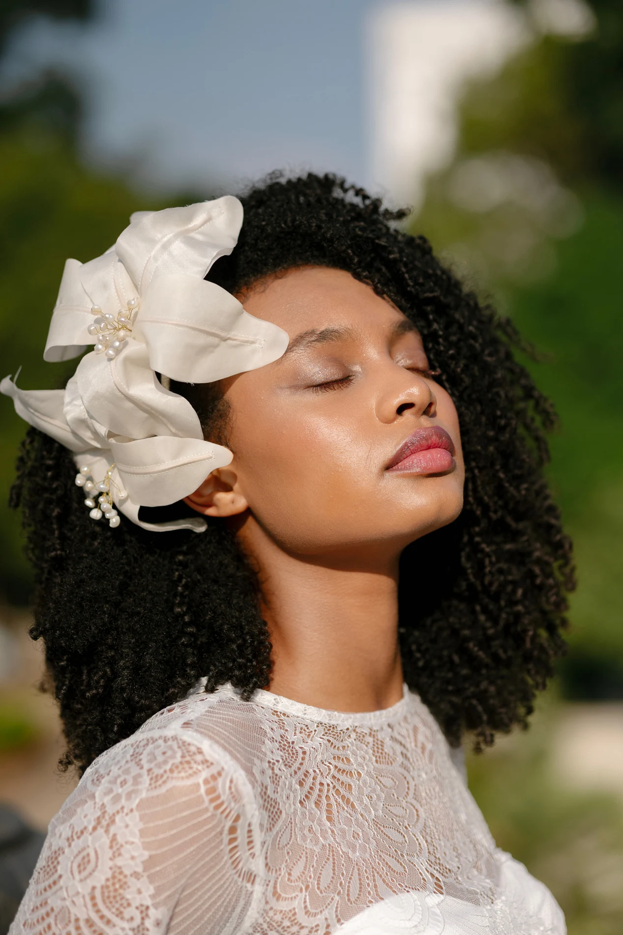 Bridal beauty portrait with dark skin, curls, and a pale floral accessory.